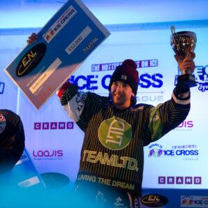 A man proudly holds a trophy, flanked by two other men, celebrating their victory in ice cross.