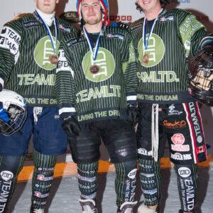 Three men in green and black uniforms prepare for an ice cross competition, showcasing teamwork and athleticism.